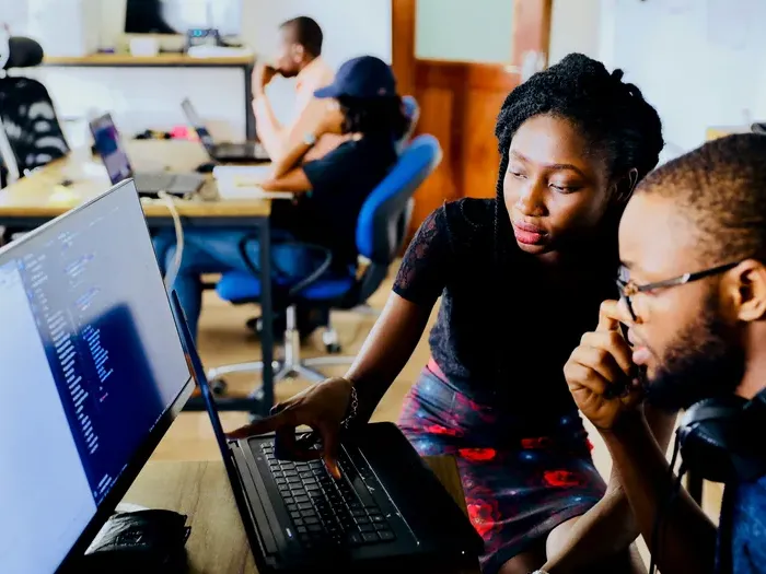 Mentor assists colleague at a computer in a shared office, showing CityBiz Spot connecting residents with reliable tech support